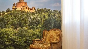 Ein Zimmer mit einer großen Wandmalerei eines historischen Gebäudes auf einem Hügel, einem alten Sessel und Holzboden.