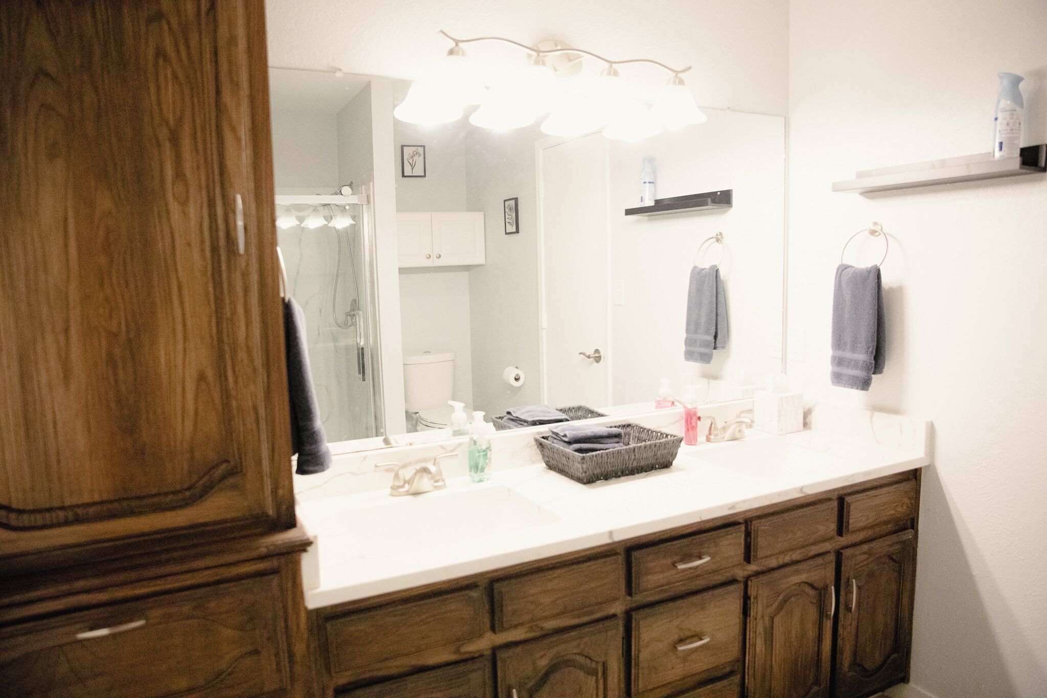Une salle de bain avec un meuble-lavabo en bois, un grand miroir et un plan de toilette blanc.