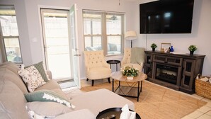 Een woonkamer met een bank, twee fauteuils, een salontafel, een open haard en een aan de muur bevestigde televisie.