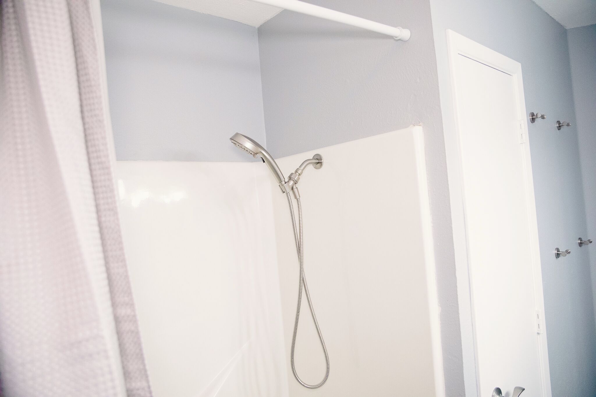 A bathroom with a shower, a white door, and a towel rack.
