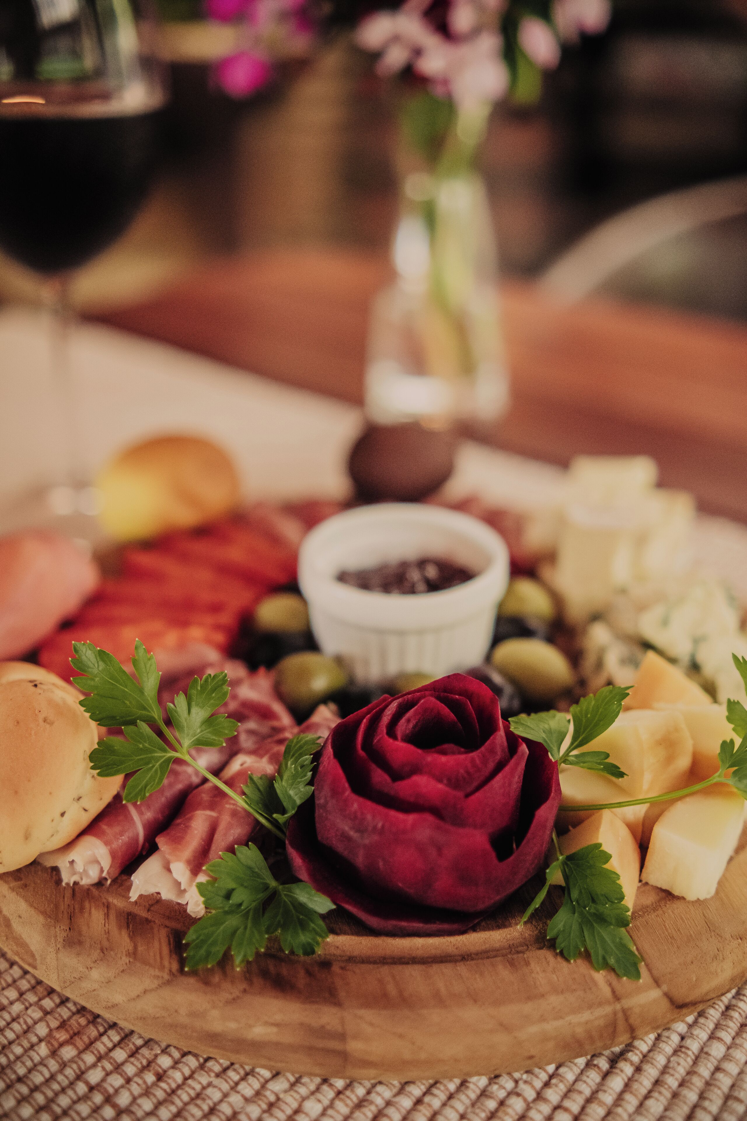 A charcuterie board with various meats, cheeses, olives, and a decorative rose on a wooden board.