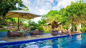 Une piscine entourée de verdure et d’un mur de pierre, avec des chaises longues et un parasol.