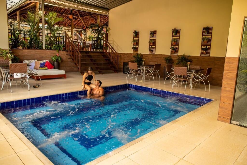 Una piscina interior con suelo de baldosas, rodeada de zonas de estar y plantas.