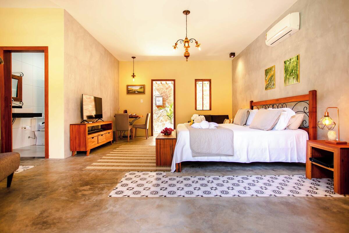 A bedroom with a bed, bedside table, lamp, and a TV in the corner.