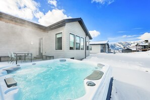 Ein verschneiter Außenbereich mit Whirlpool, einem Esstisch mit Stühlen und einem Gebäude mit großen Fenstern.