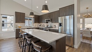 Una cocina moderna con una isla grande, electrodomésticos de acero inoxidable, armarios de madera oscura e iluminación colgante.