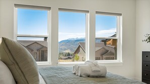 Un dormitorio con cama, dos ventanas y vistas a casas y montañas.
