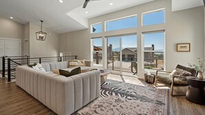 Un salón amplio con un sofá seccional grande, un tapete estampado con motivos de cebra y vistas al exterior a través de amplias ventanas.