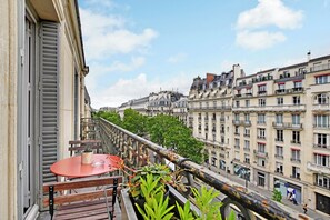 A balcony with a table and chairs, overlooking a city street with buildings and trees. - Appartement de Luxe 2 Chambres Avec Balcon à Trocadéro (Paris)