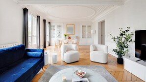 Un salon moderne avec un canapé bleu, des fauteuils blancs, une table basse et un téléviseur.