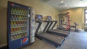 Ein Fitnessbereich mit Laufbändern, einem Kraftgerät und einer Pepsi-Getränkeautomaten.