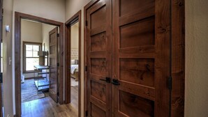 Ein Flur mit Holztüren, der zu einem Schlafzimmer mit Bett und Fenster führt.