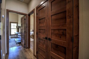 Un couloir avec des portes en bois menant à une chambre à coucher qui contient un lit et une fenêtre.
