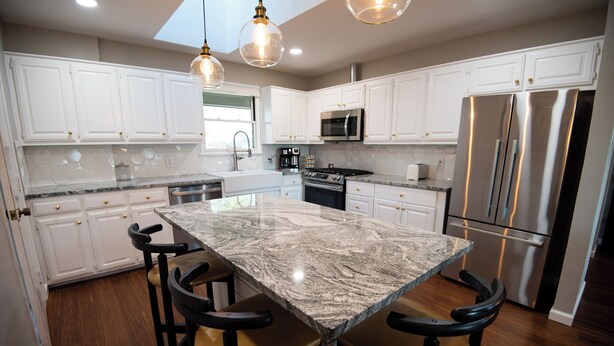 Una cocina moderna con armarios blancos, una isla grande con taburetes de bar, electrodomésticos de acero inoxidable e iluminación colgante.