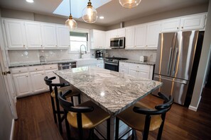 A modern kitchen with white cabinets, a large island with bar stools, stainless steel appliances, and pendant lighting.