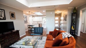 Una sala de estar moderna con un sofá, una mesa de centro de vidrio y un televisor sobre un mueble de madera.