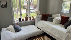 Un dormitorio con un ventanal grande, un sofá, una cama y varias macetas con plantas en el alféizar.