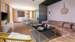 A modern living room with a sofa, a coffee table, a TV, and a dining area with chairs and a table. - Amazing home in Mihatovici (Mihatovici)