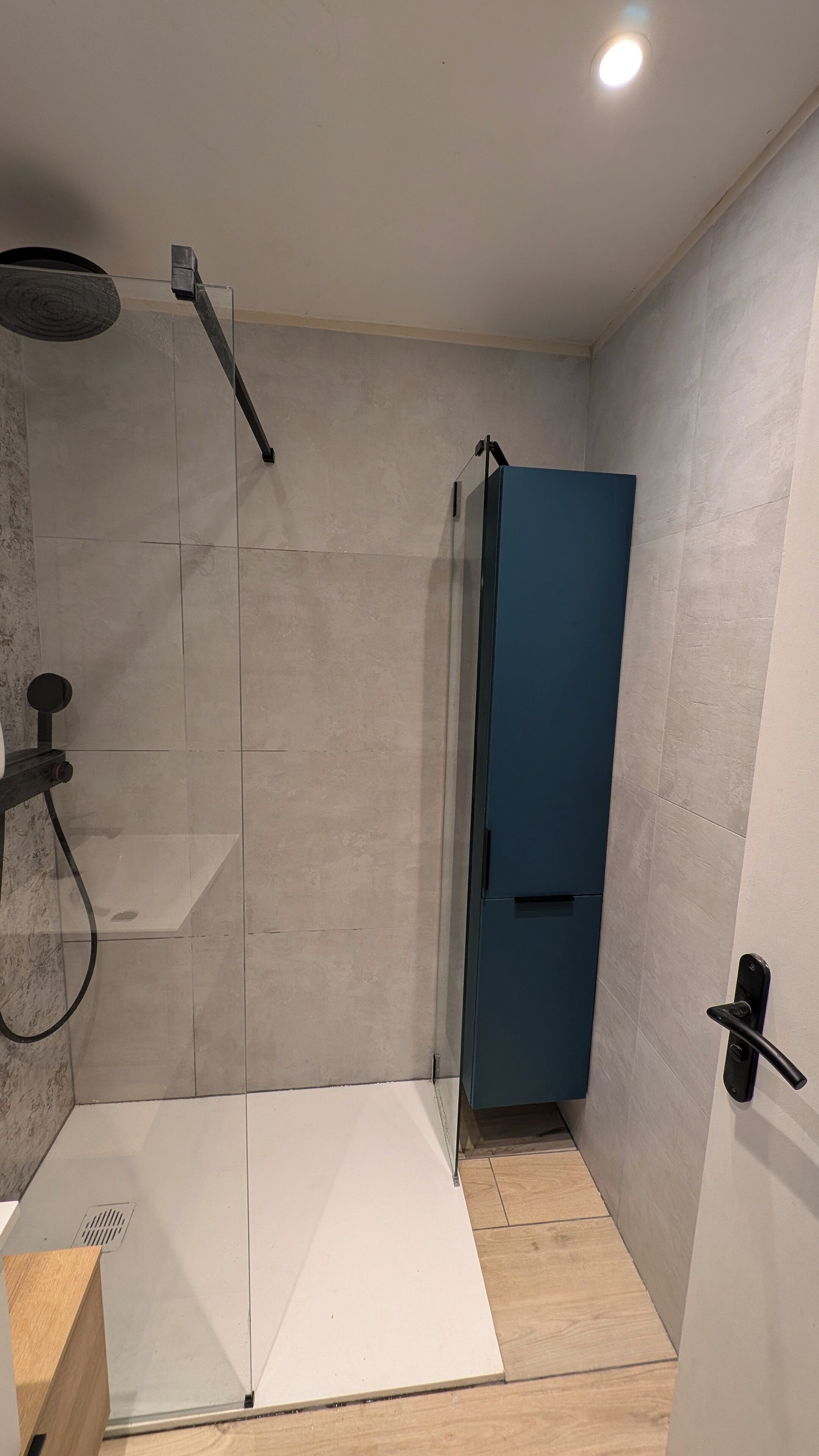 A modern shower area with a glass door, a wooden floor, and a light fixture on the ceiling.