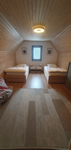 A small attic bedroom with two beds, a window, and a ceiling light.