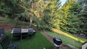 An outdoor patio with a table and chairs, surrounded by trees and a grill. - Gite "Les Myrtilles (Laguiole)