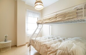 A bunk bed room with a ladder, a small table with a vase, and a window with curtains.
