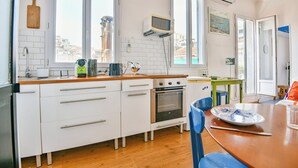 Et lille køkken med hvide skabe, indbygget ovn, mikroovn og kaffemaskine.