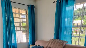 Ein beiges Ecksofa mit gerippten Kissen, ein Fenster mit blauen Vorhängen und ein Fliesenboden.