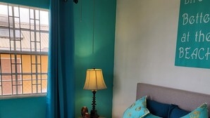 Ein Schlafzimmer mit türkisfarbenen Wänden, einer blumigen Bettdecke und einem Wandschild mit der Aufschrift 'Life is better at the beach'.
