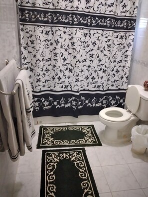 A bathroom with a white toilet, a black and white patterned shower curtain, and a black and white patterned bath mat.