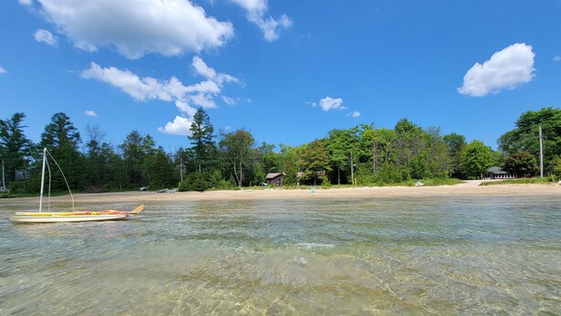 A beach with clear water, a canoe, and a house in the background.