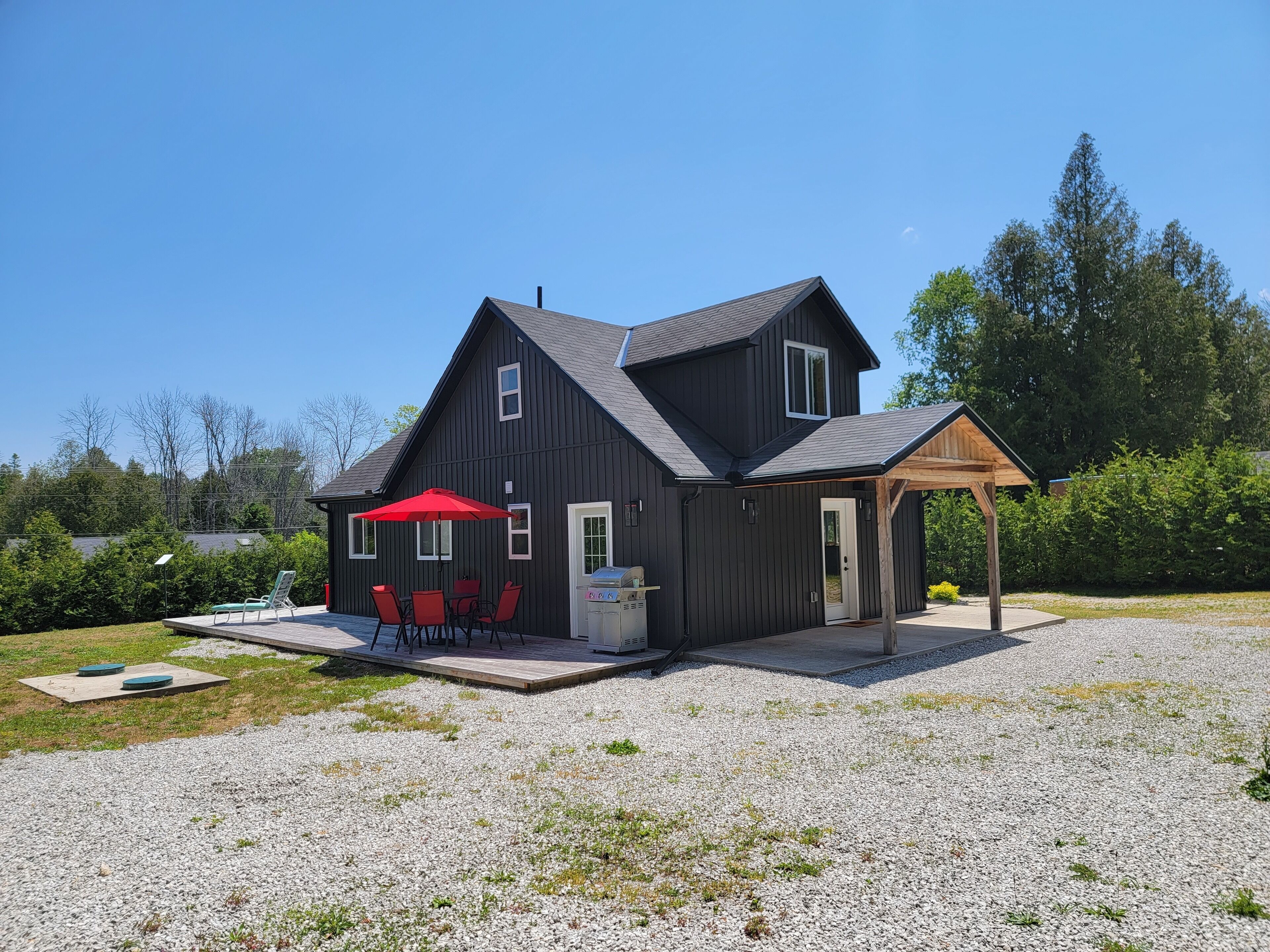 Une maison à deux étages dotée d’un patio comprenant un parasol rouge, des sièges d’extérieur et un barbecue.