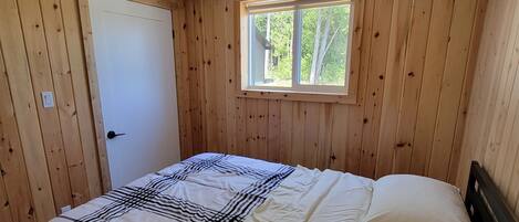 Een slaapkamer met een bed, een plafondventilator, een raam en houten wanden.