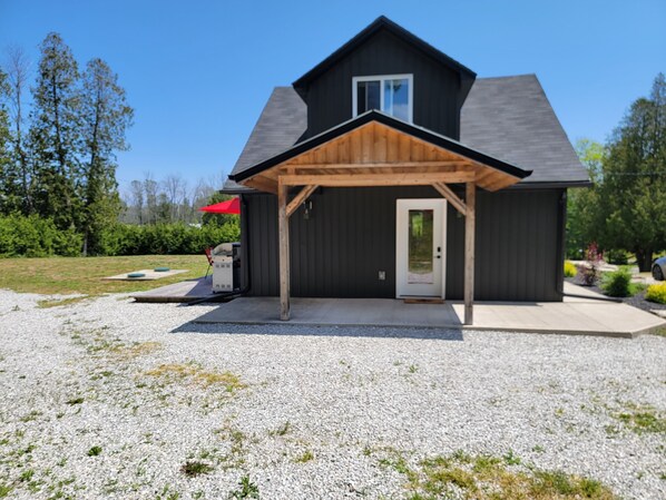 A modern house with a covered porch, a gravel driveway, and a red umbrella.