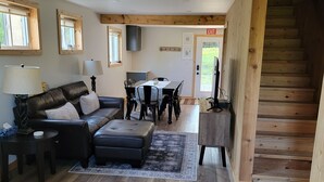 A spacious living area with a wooden staircase, a sofa set, a dining table, and a kitchen area.