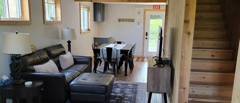 A spacious living area with a wooden staircase, a sofa set, a dining table, and a kitchen area.