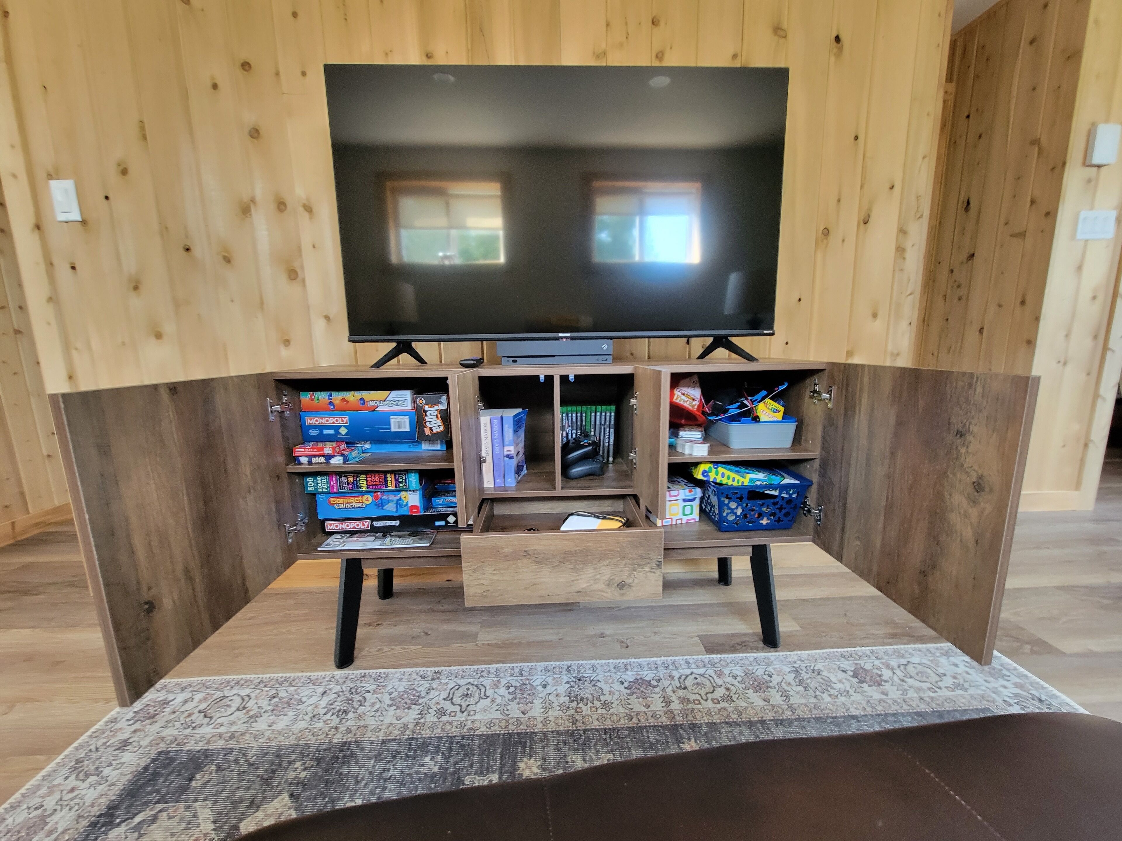 Un meuble de rangement en bois comprenant un téléviseur à écran plat, des étagères pour les jeux de société et des tiroirs de rangement.