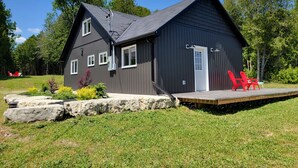A two-story building with a dark exterior, a flat roof, and a small porch with red chairs.