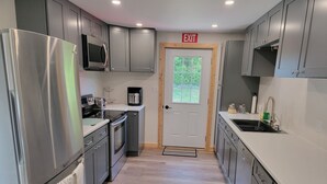 A modern kitchen with grey cabinets, stainless steel appliances, a built-in microwave, a coffee maker, and a sink.