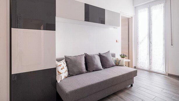 A modern living room with a grey sofa, a flat-screen TV mounted on the wall, and a sliding glass door leading to a balcony. - Appartamento a Piazza dell'Unità by Wonderful Italy (Bologna)