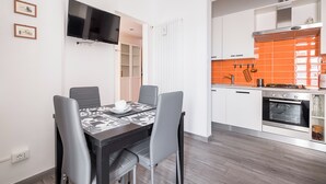 A modern kitchen with white cabinets and an orange backsplash, a dining area with a black table and gray chairs, and a flat-screen TV mounted on the wall. - Appartamento a Piazza dell'Unità by Wonderful Italy (Bologna)