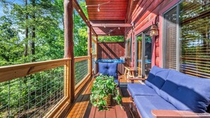 A wooden deck with a blue sofa, a table with a plant, and a hot tub. - Rustic Pigeon Forge Cabin - Mountain View/King Beds/Hot Tub/Minutes to Dollywood (Sevierville)