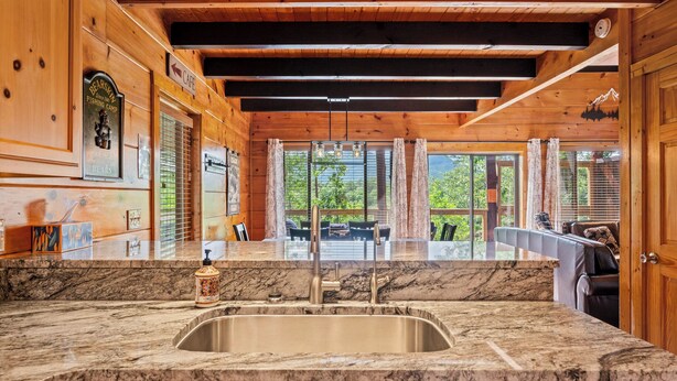 A kitchen with a marble countertop, stainless steel sink, wooden cabinets, and a view of the outdoors. - Rustic Pigeon Forge Cabin - Mountain View/King Beds/Hot Tub/Minutes to Dollywood (Sevierville)