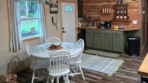 A dining area with a wooden ceiling, a chandelier, a white table with chairs, a kitchen in the background, and a window with curtains. - Family lake escape! Huge deck/BBQ/fire pit. Bunk room. 5 min to boat ramp! Pets! (Cadiz)
