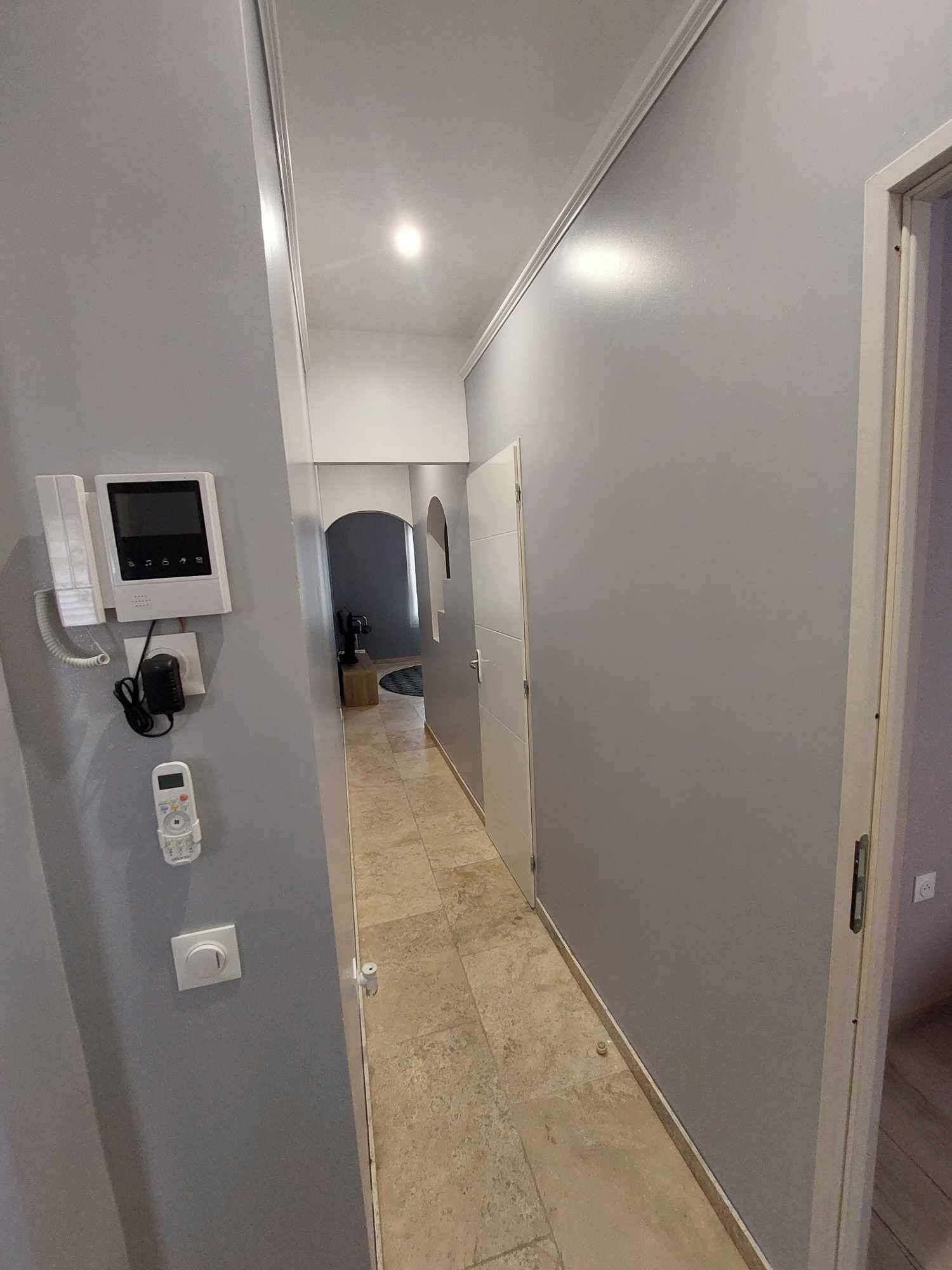 Un couloir étroit aux murs gris, doté d’un sol carrelé et d’une porte au fond.