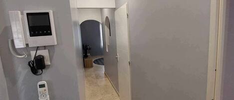 Un couloir étroit aux murs gris, doté d’un sol carrelé et d’une porte au fond.