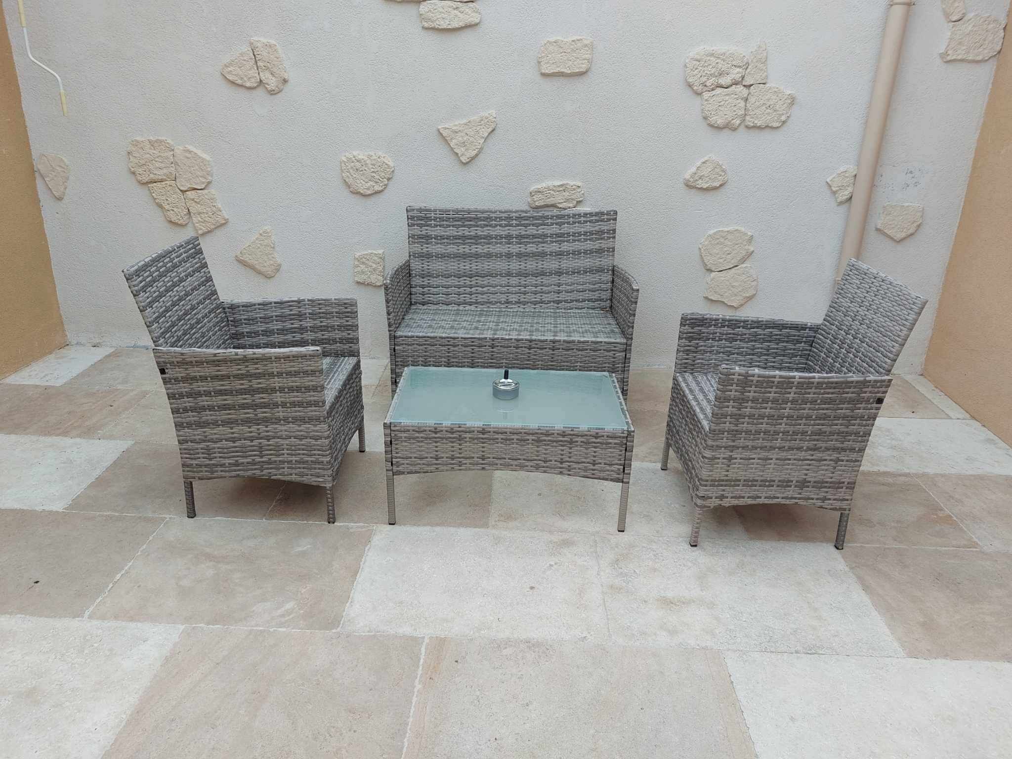 A patio area with three wicker chairs and a small table, set against a textured wall with stone-like decorations.