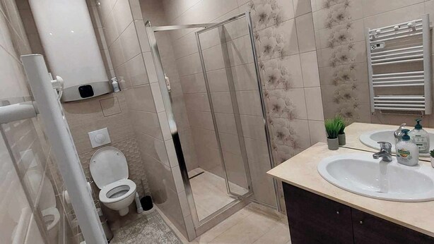 A modern bathroom with a glass shower enclosure, a toilet, a sink with a mirror above it, and a towel rack. - Charmant Appartement (Tarascon)