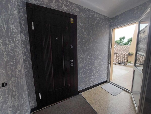 A dark wooden door with a textured wall, a glass door leading outside, and a small mat at the entrance. - Charmant Appartement (Tarascon)