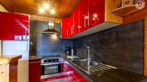 A modern kitchen with red cabinets, stainless steel appliances, and a black countertop. - L'oree DU Bois - Arole (VAL CENIS)